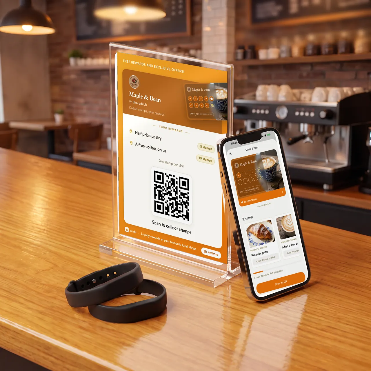 An Ambr counter stand, a phone showing the loyalty card, and two stamping wristbands on a café counter