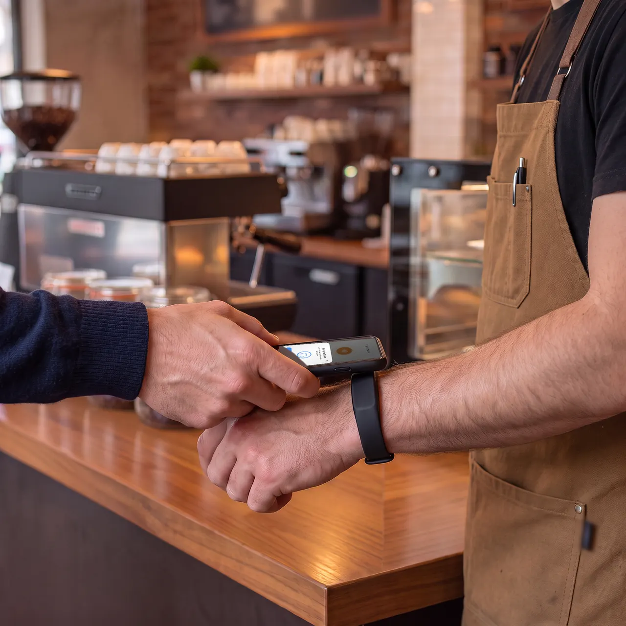 A customer taps their phone on the barista’s stamping wristband at the counter